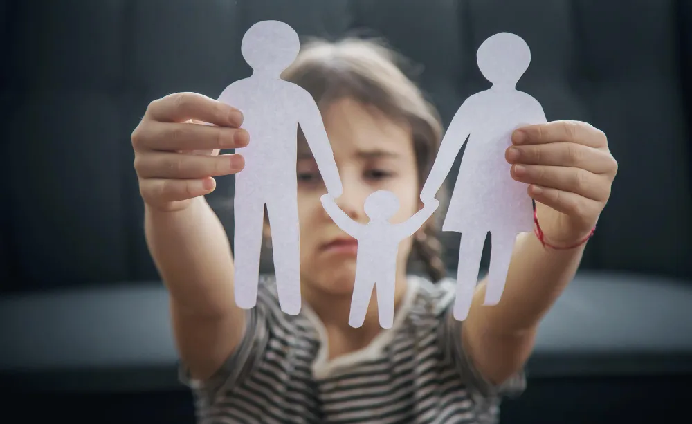 Criança triste segura figuras de papel, buscando o que fazer sobre alienação parental.