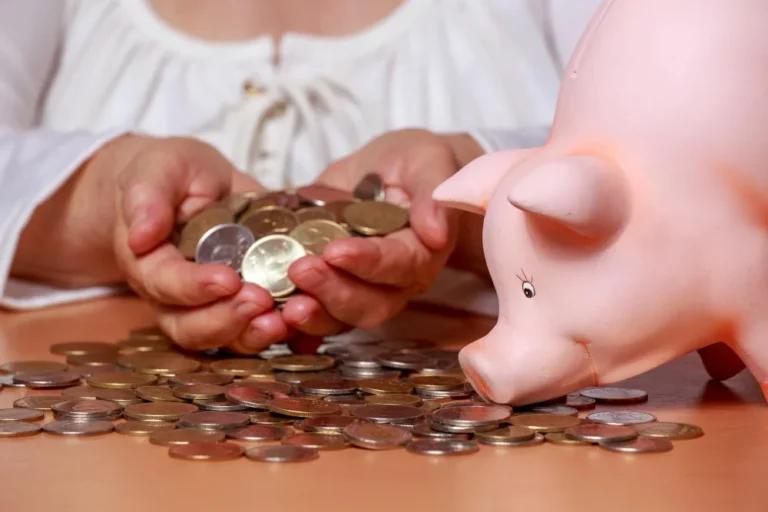 Mãos segurando moedas perto de um cofrinho, sobre revisão de pensão alimentícia como pedir.