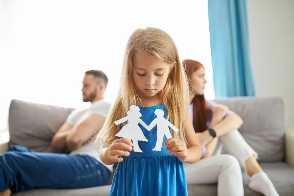 Menina segura recortes de papel representando pais, simbolizando divórcio com filhos menores.