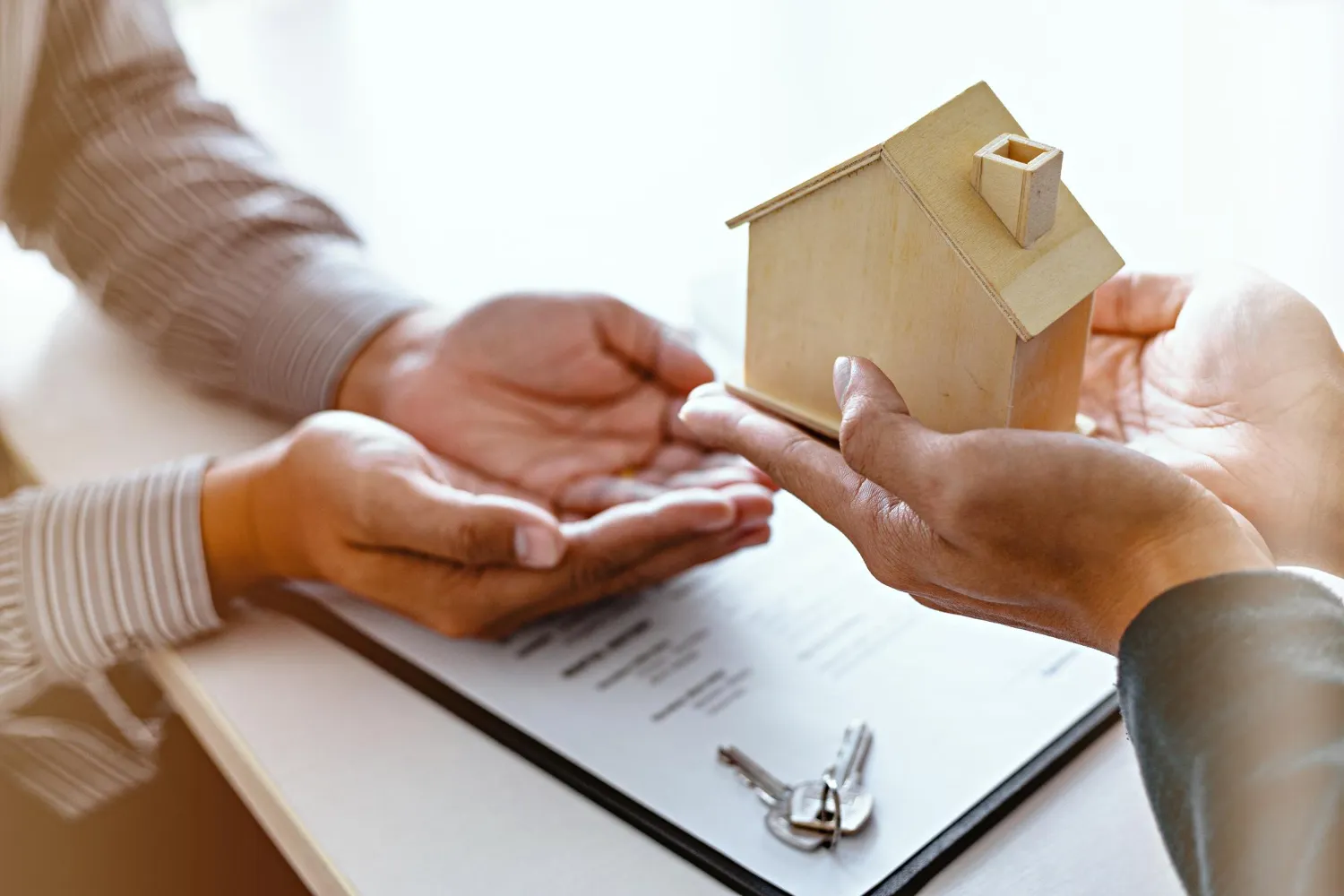 Mãos entregando miniatura de casa, discutindo quem tem direito a herança.